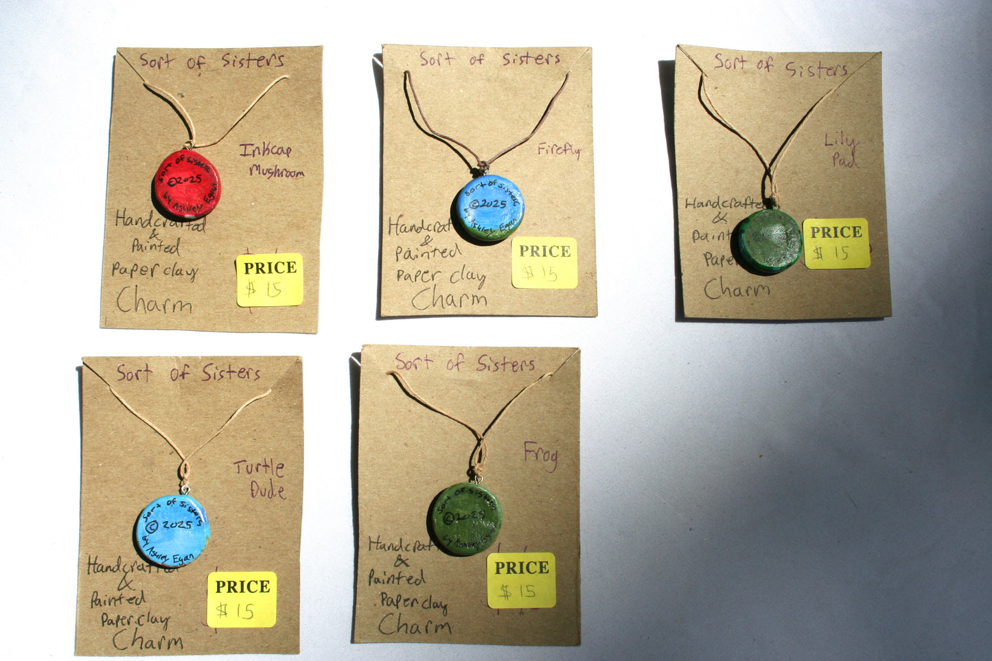 The back of all charms, each has Sort of Sisters at the top, the year in the middle, and by Ashley Egan at the bottom.