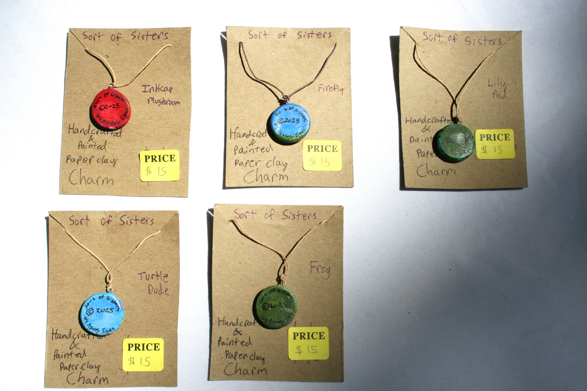 The back of all charms, each has Sort of Sisters at the top, the year in the middle, and by Ashley Egan at the bottom.