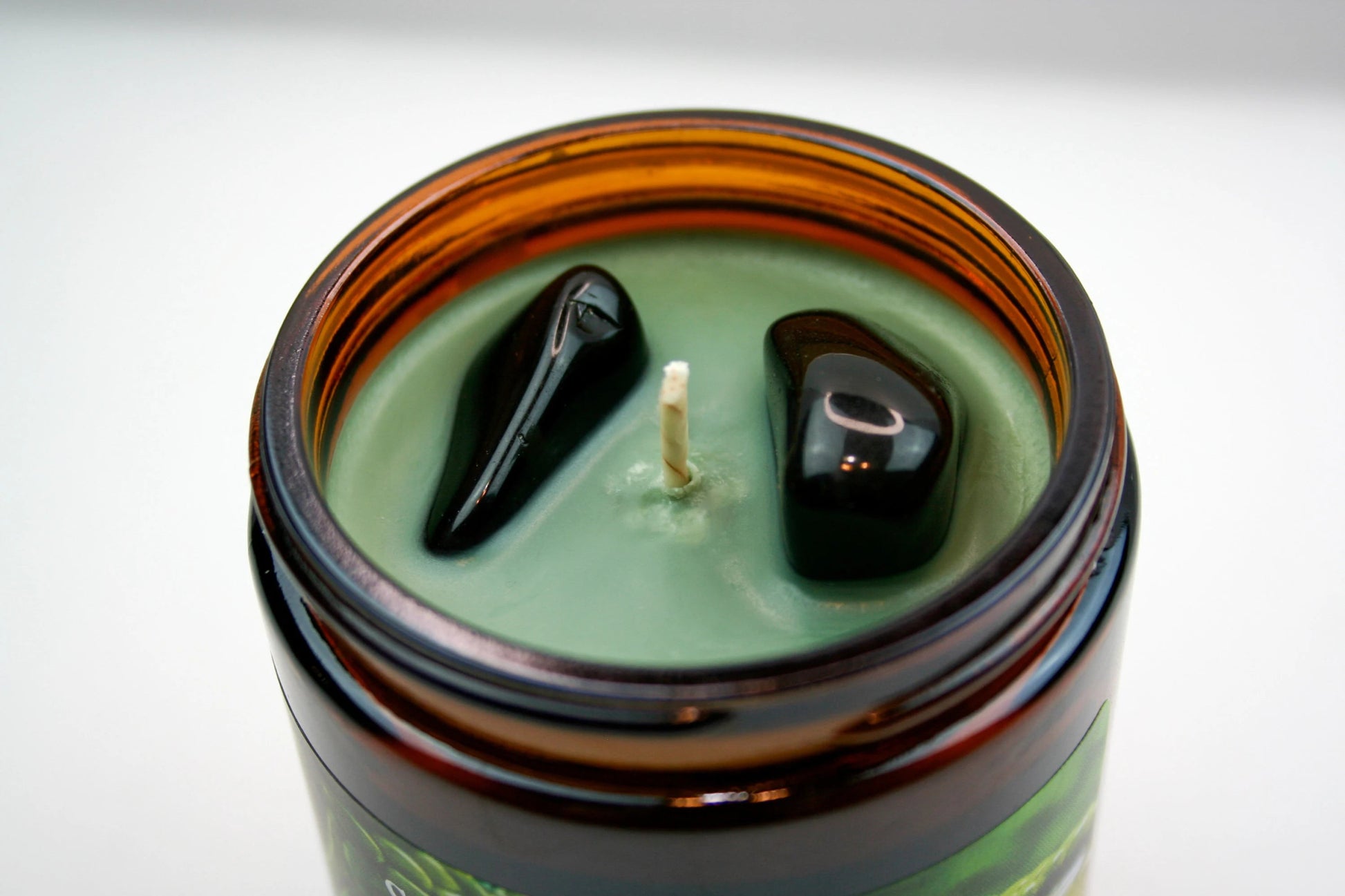 A close up of the top of our "Loki" candle, featuring the pale Kelley green wax and two black obsidian stones.