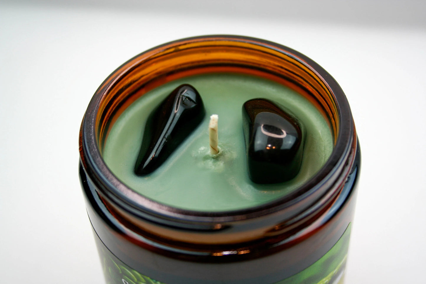 A close up of the top of our "Loki" candle, the image shows the Kelley green wax and two black obsidian stones.